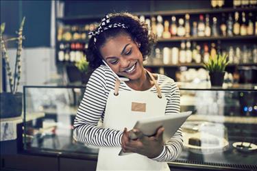 happy female restaurant manager on the phone while looking at her tablet