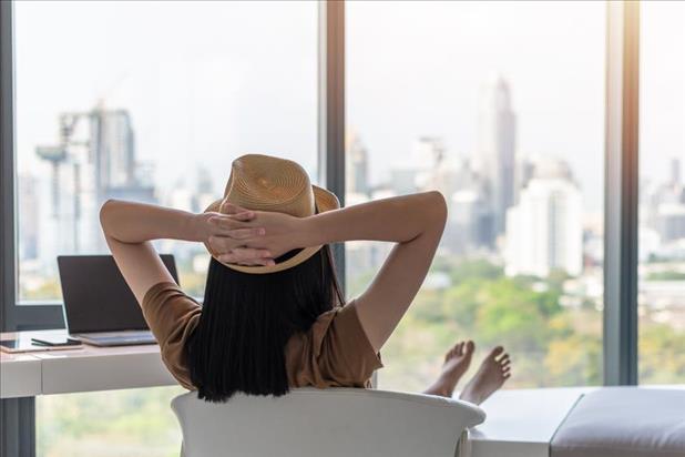 Woman with hat and bare feet relaxing in office chair while looking out window