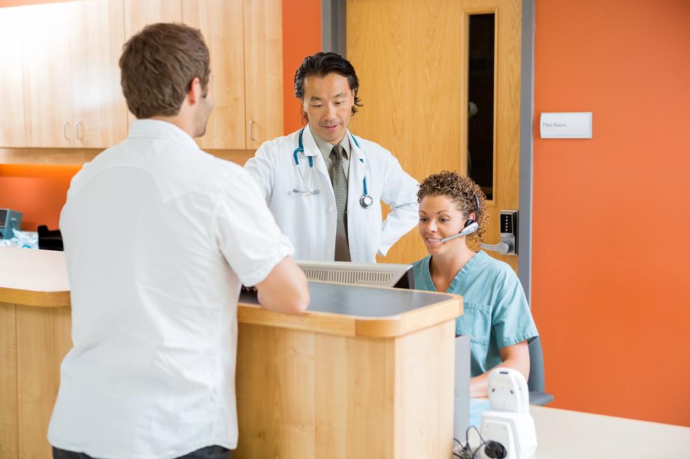 medical receptionist behind her desk with a doctor and a patient in front of them