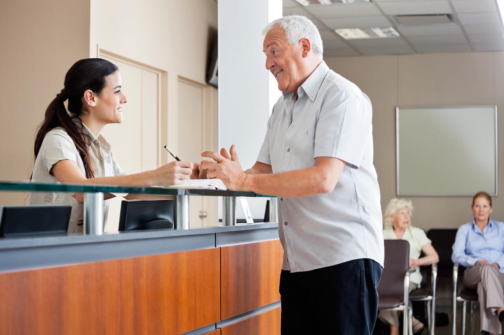 medical office administrator assisting a patient at the front desk