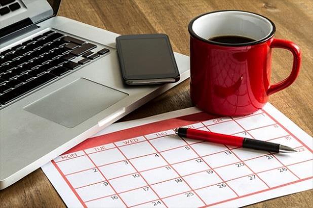 Laptop, phone, coffee cup, and calendar sitting on a desk