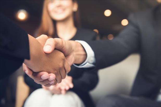 two people shaking hands with a smiling person in the background