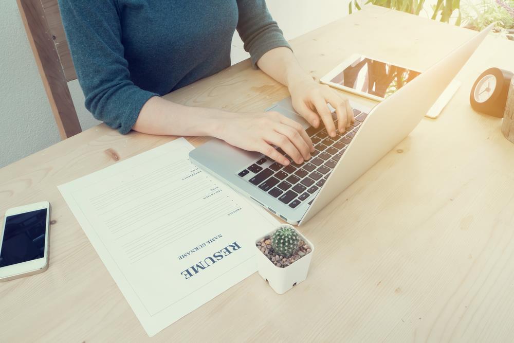 job seeker at desk reviewing resume with laptop