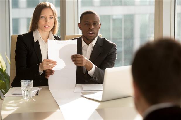 two interviewers holding a long resume staring at a candidate in shock