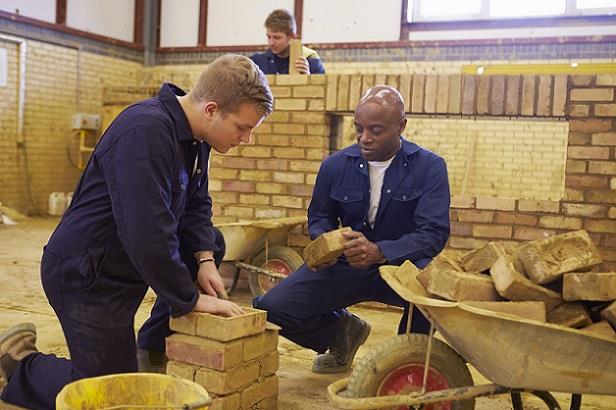 Apprentice bricklayer learning on the job from an experienced mason