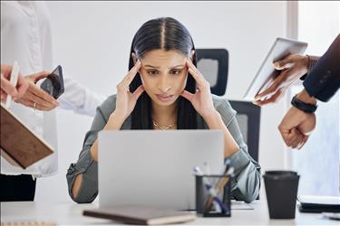 overwhelmed employee at her desk with tasks coming in from all directions