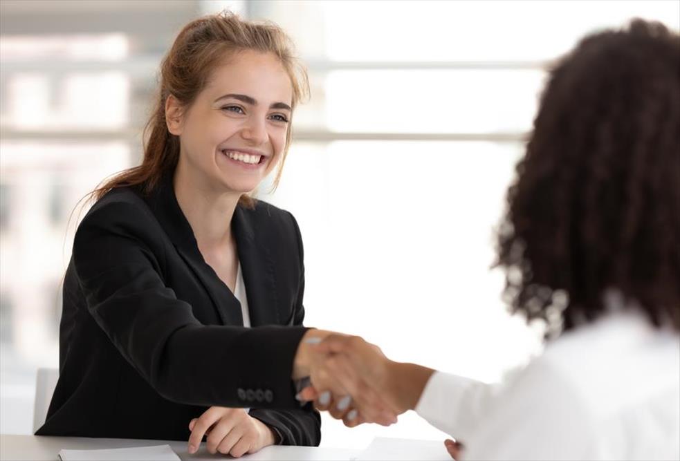 Jovial, blonde woman smiles and shakes hands with employer after accepting a job offer she earned thanks to her strong, authentic personal brand.