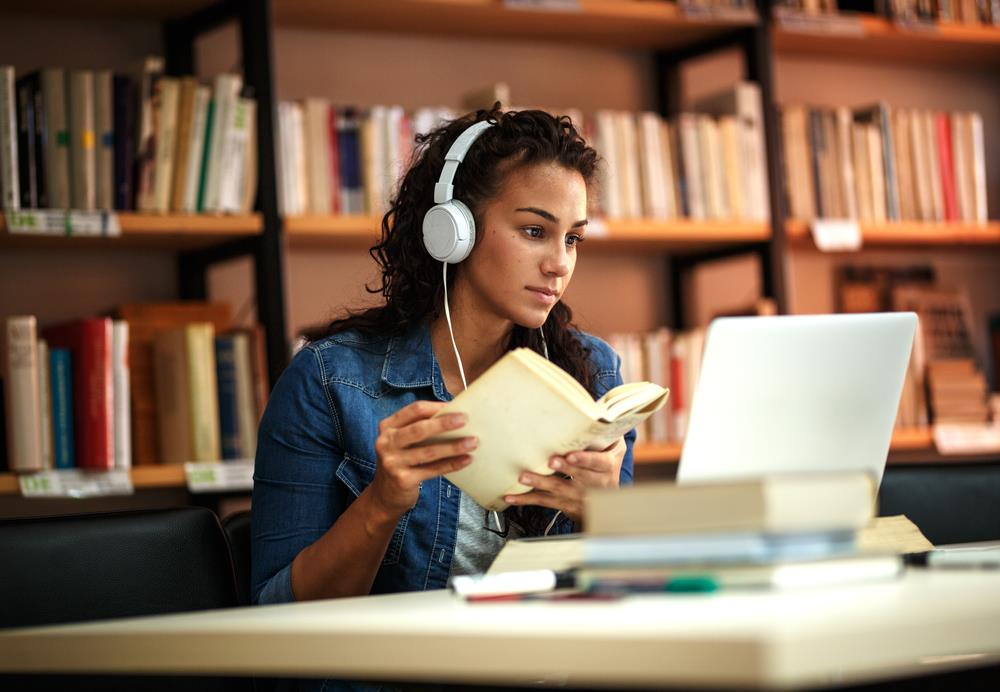 Job seeker wearing headphones sits in library, doing research on her computer as she embraces learning as the best pathway to growth and flexibility.