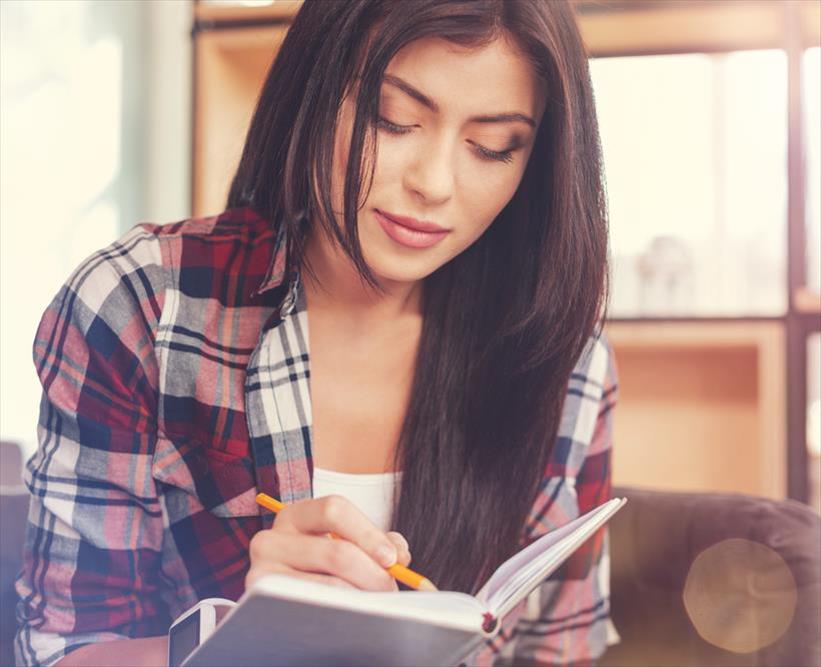 Casually dressed young woman is writing her self-description in a notebook as inspiration for her personal brand.