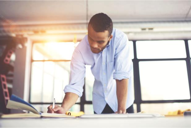 man standing over desk writing