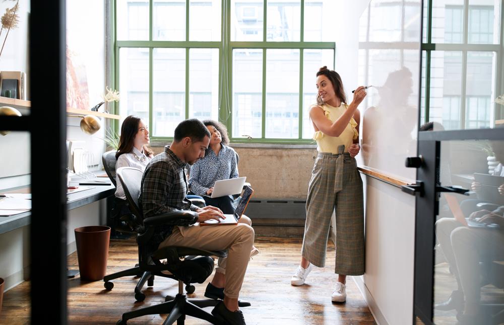 Woman writing on whiteboard while discussing with colleagues