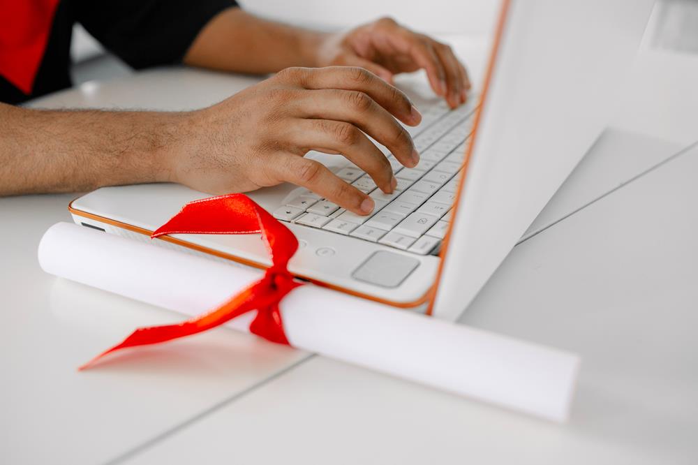 new grad searching for jobs on his laptop with his diploma on the table