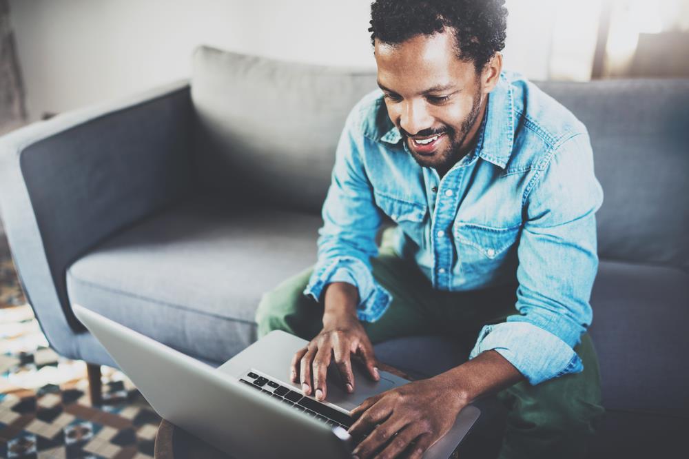 Smiling African American man sitting on couch looking at a laptop