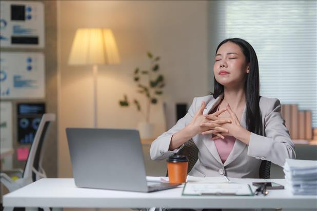 office worker meditating at her desk with her eyes closed