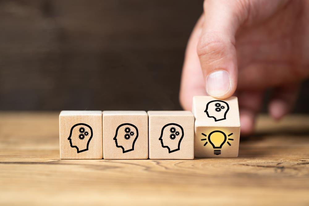 "idea" concept with four wooden cubes with heads on them in a row. one is being turned over to show a yellow light bulb.