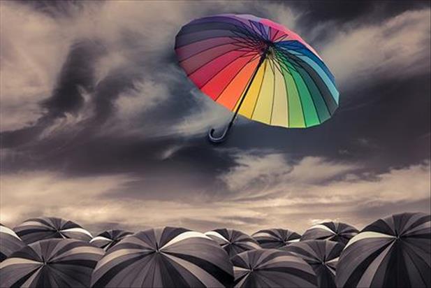 Colorful umbrella floating above group of dark colored umbrellas