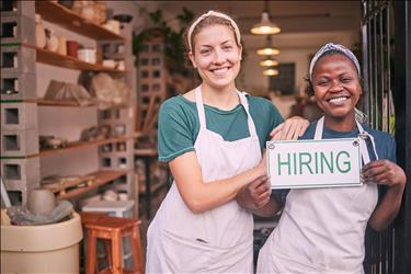 two retail store workers holding a hiring sign