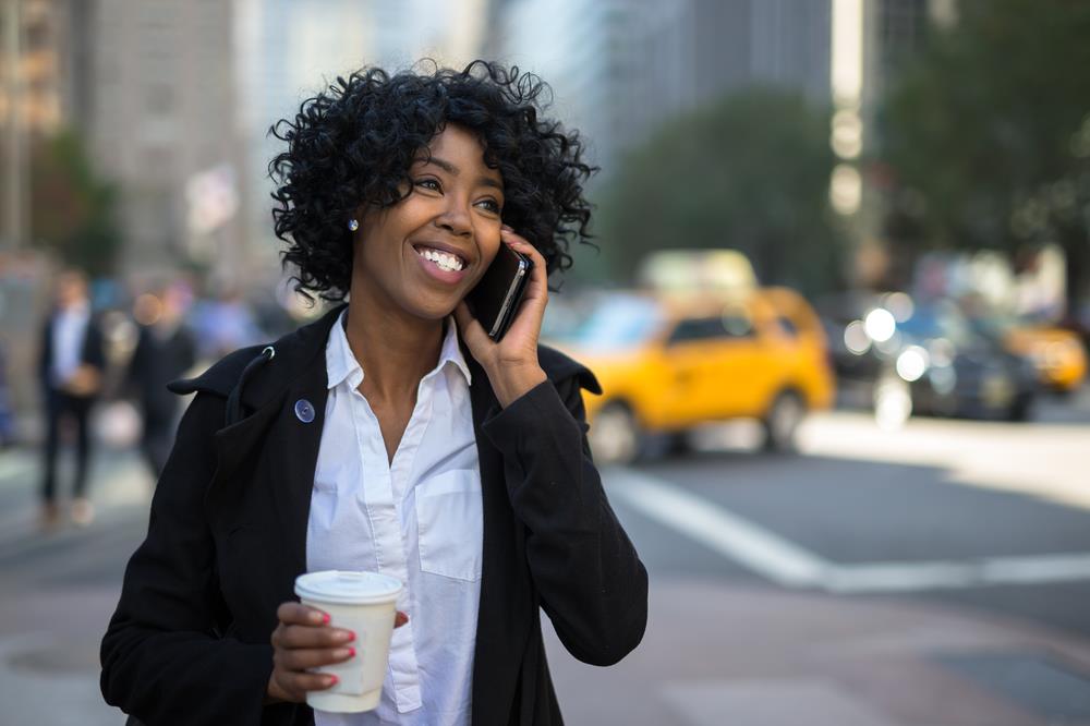 professional with multiple part-time jobs drinking coffee on the go while talking to one of her bosses on the phone