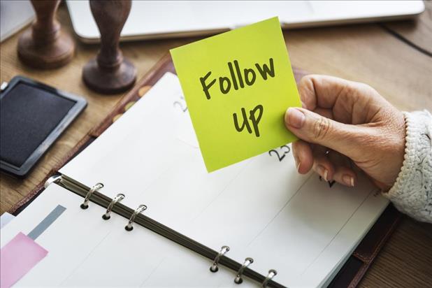 Woman holding reminder sticky note that says "Follow Up"