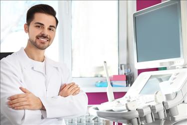 smiling diagnostic medical sonographer standing in front of his equipment in the exam room