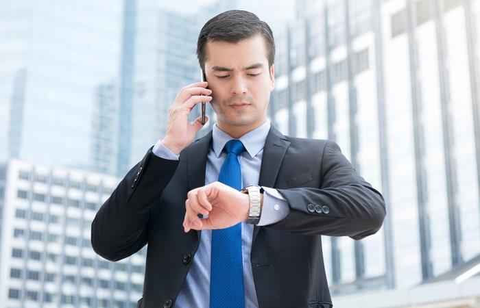 Businessman calling interviewer and looking at his watch