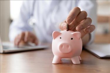 medical pro putting money into a piggy bank while working on their laptop