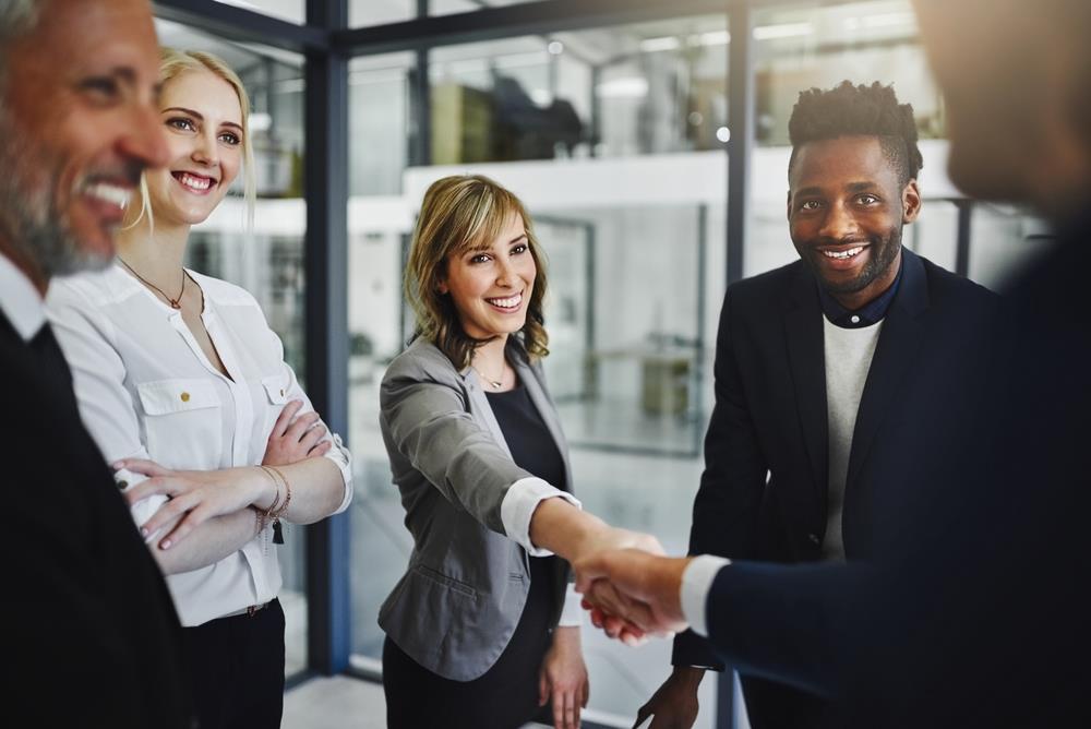 new hire shaking hands with her new boss with other smiling people around