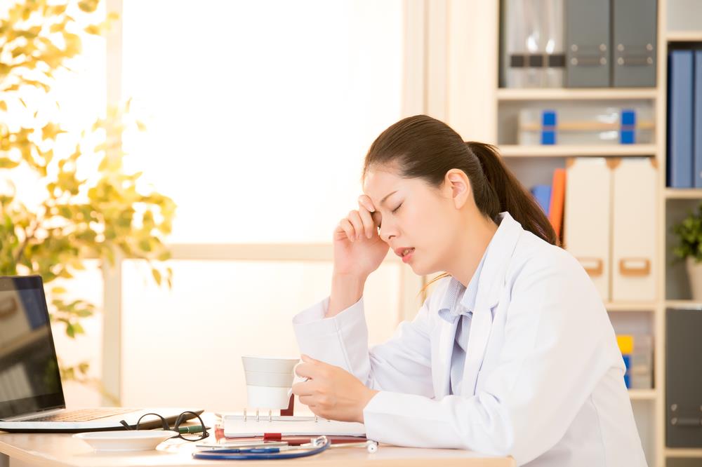 Stressed out optometrist sitting at desk and suffering from doctor burnout