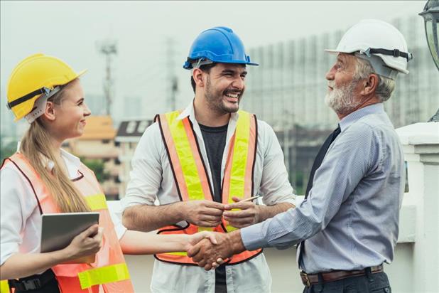 construction worker shaking a client's hand with a team member smiling at him