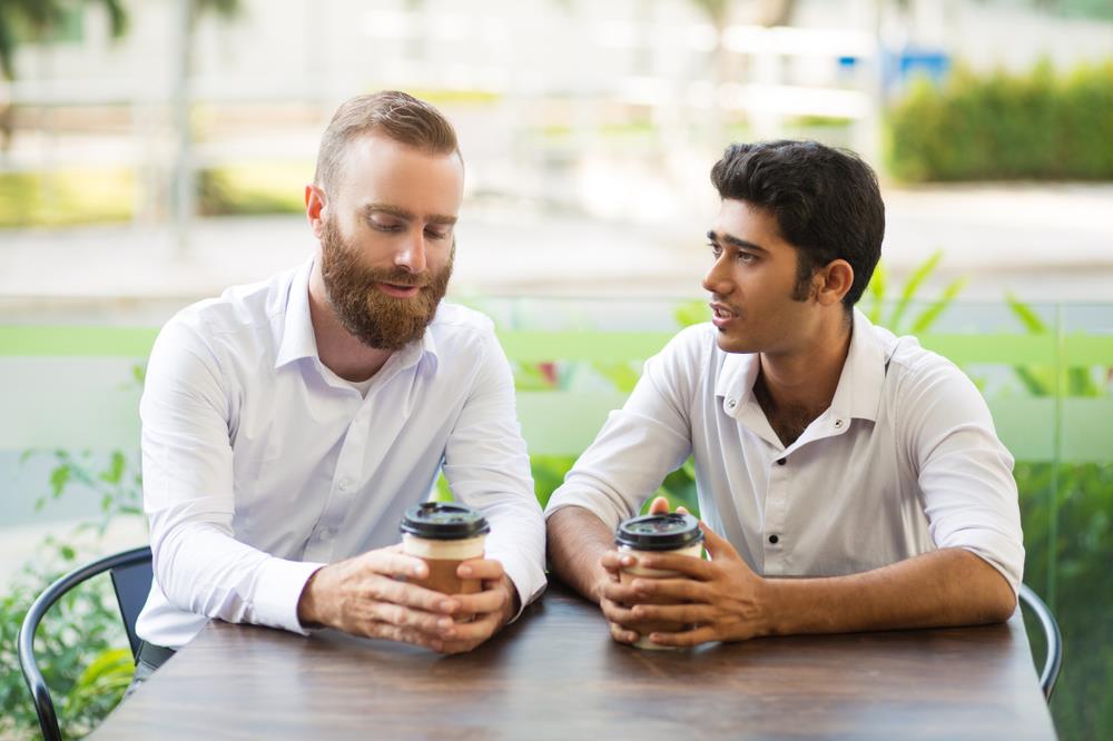 two friends talking about job loss at an outdoor cafe