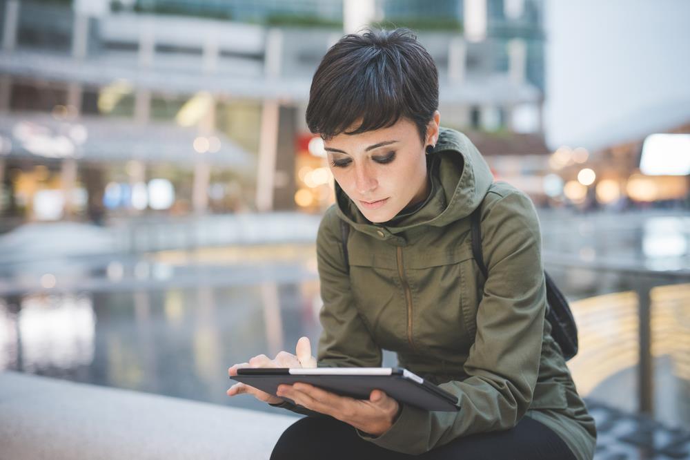 Young woman sitting outside and looking at her email on a tablet