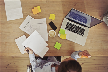 Top view of woman in front of laptop surrounded by papers while working on her resume