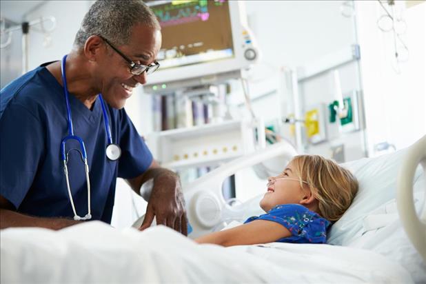 Male nurse laughing with little girl in hospital bed