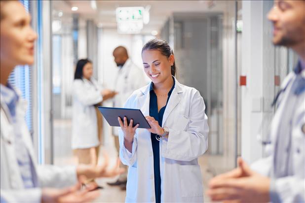 doctor smiling while looking at her tablet with other staff in the hallway