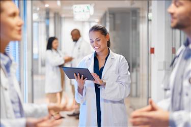 doctor smiling while looking at her tablet with other staff in the hallway