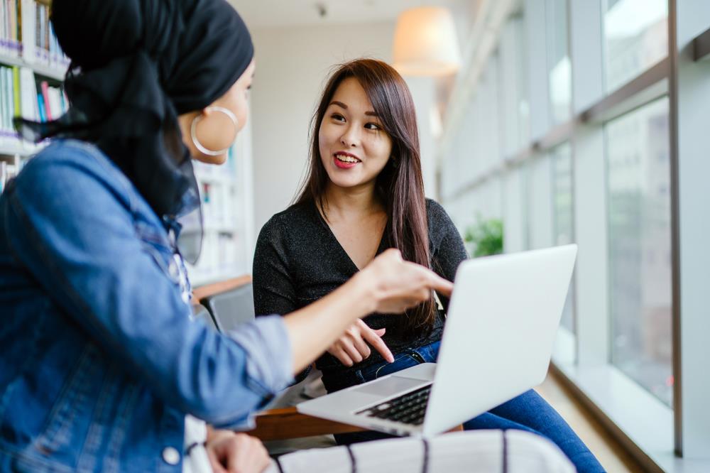 Manager referencing laptop while speaking with her employee about her performance