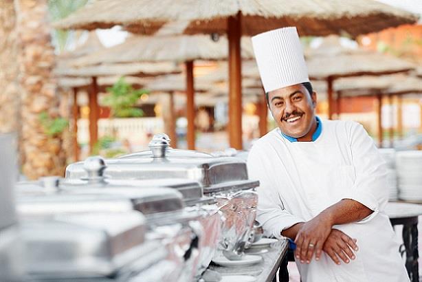 Happy chef posing in front of buffet at a tropical resort