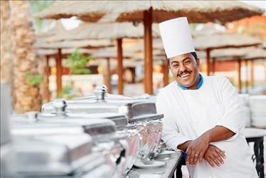 Happy chef posing in front of buffet at a tropical resort