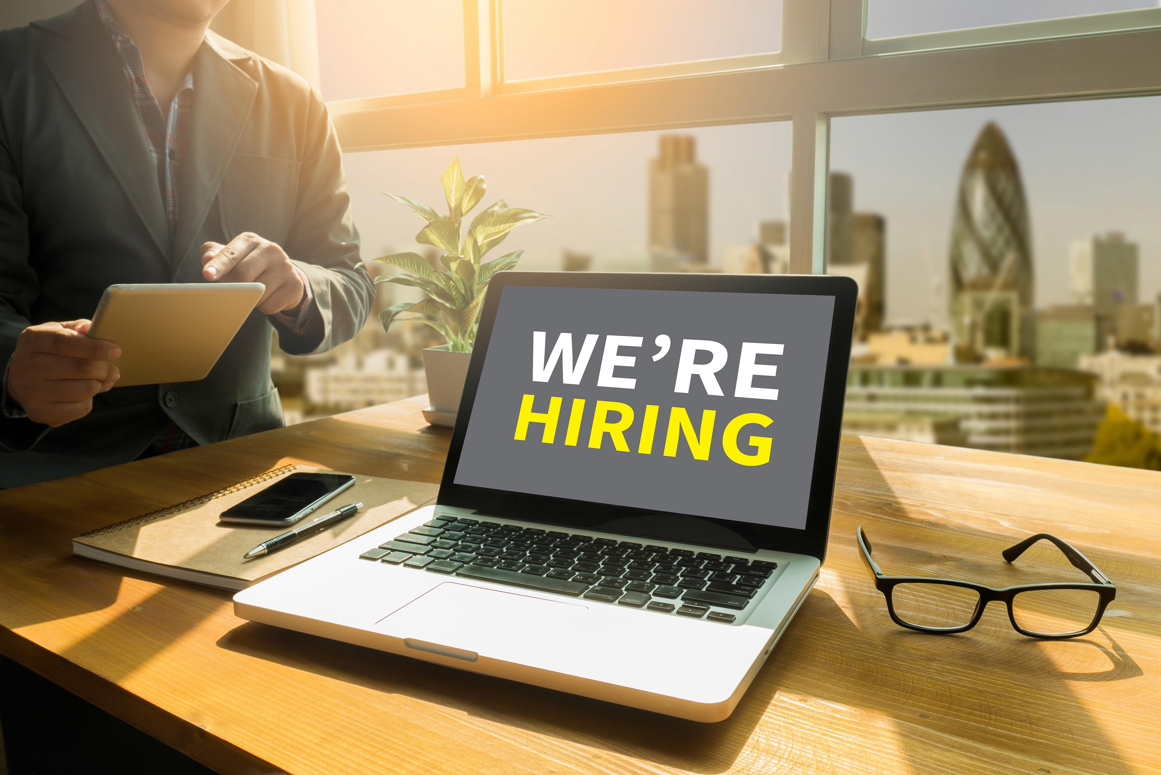 laptop on a desk with the words "we're hiring" on the screen