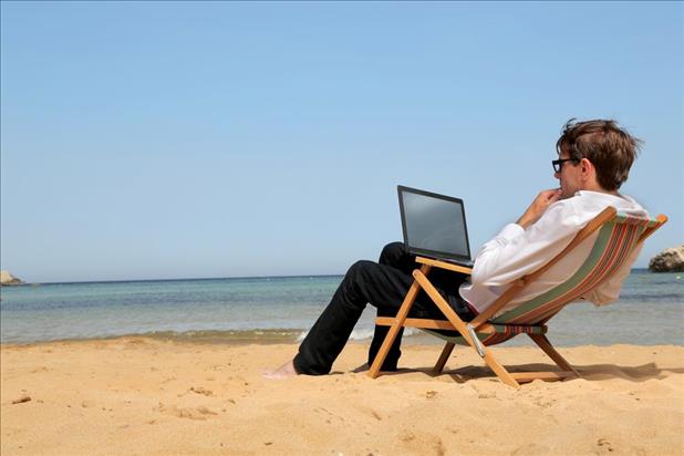 Man at the beach searching for jobs on his laptop