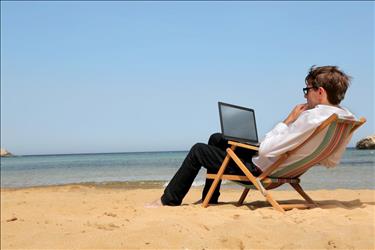 Man at the beach searching for jobs on his laptop