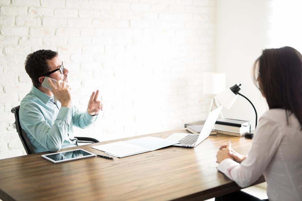 Man taking phone call signaling for candidate to wait during interview