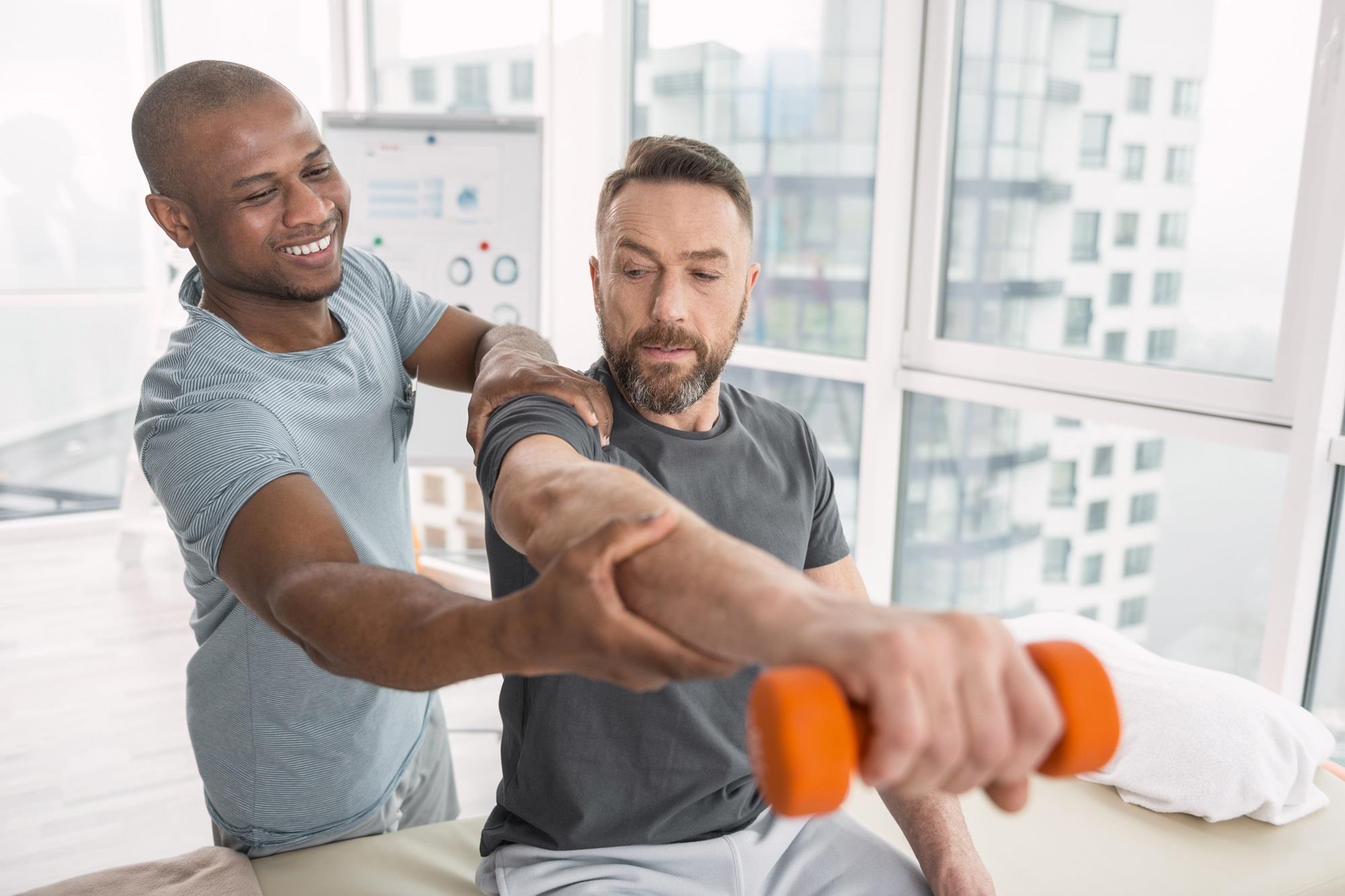 physical therapist assisting his patient with arm exercises