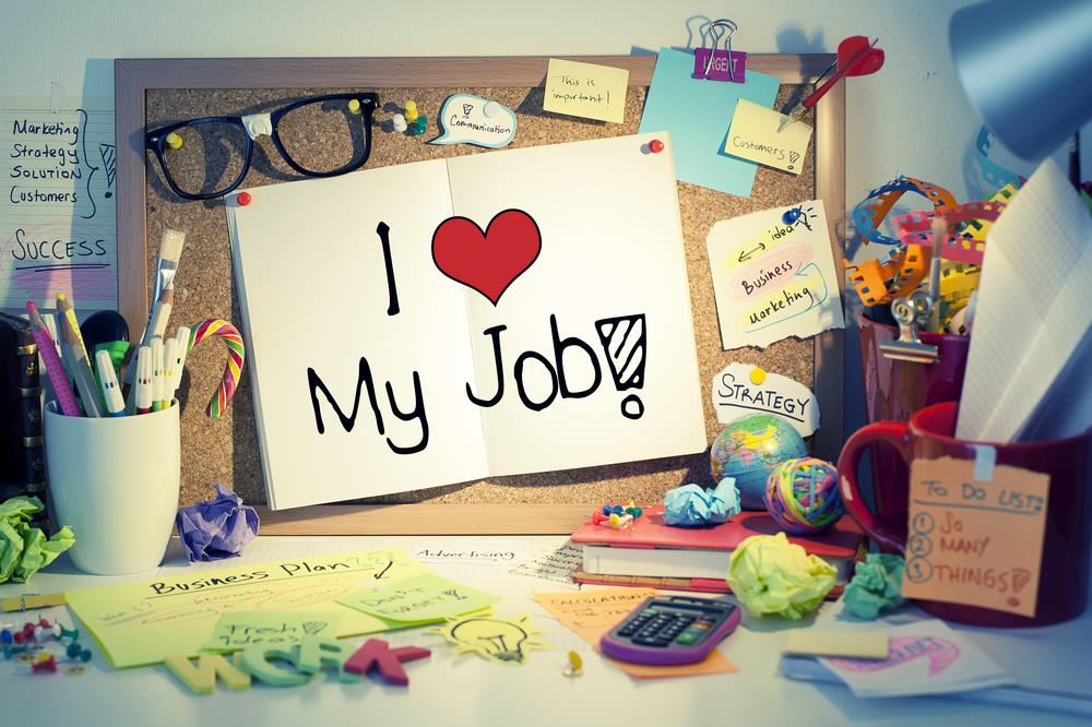 busy desk with "i love my job" posted on the bulletin board