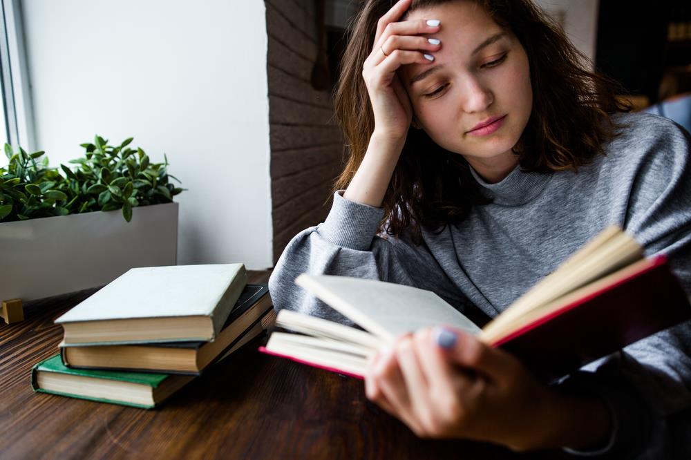 Undergraduate student reading books next to a window