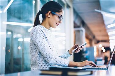 Woman checking phone while working on computer