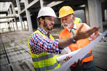 Older construction professional with younger employee on job site