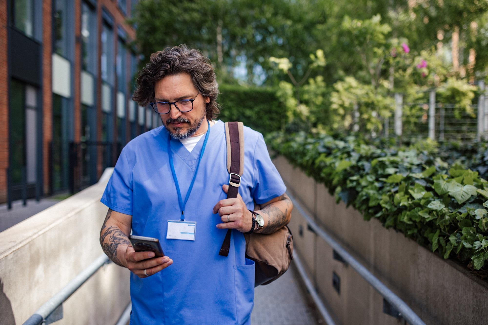 healthcare worker checking his phone while walking outside
