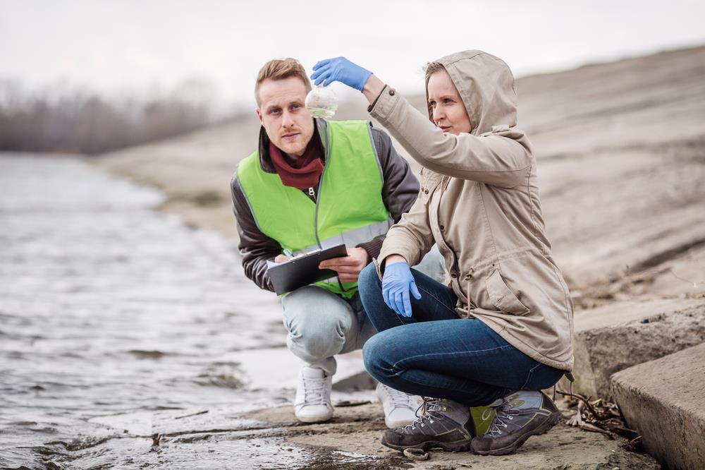 female environmental scientist testing river water with her male partner taking notes