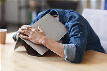 frustrated employee covering his head on a table with his laptop